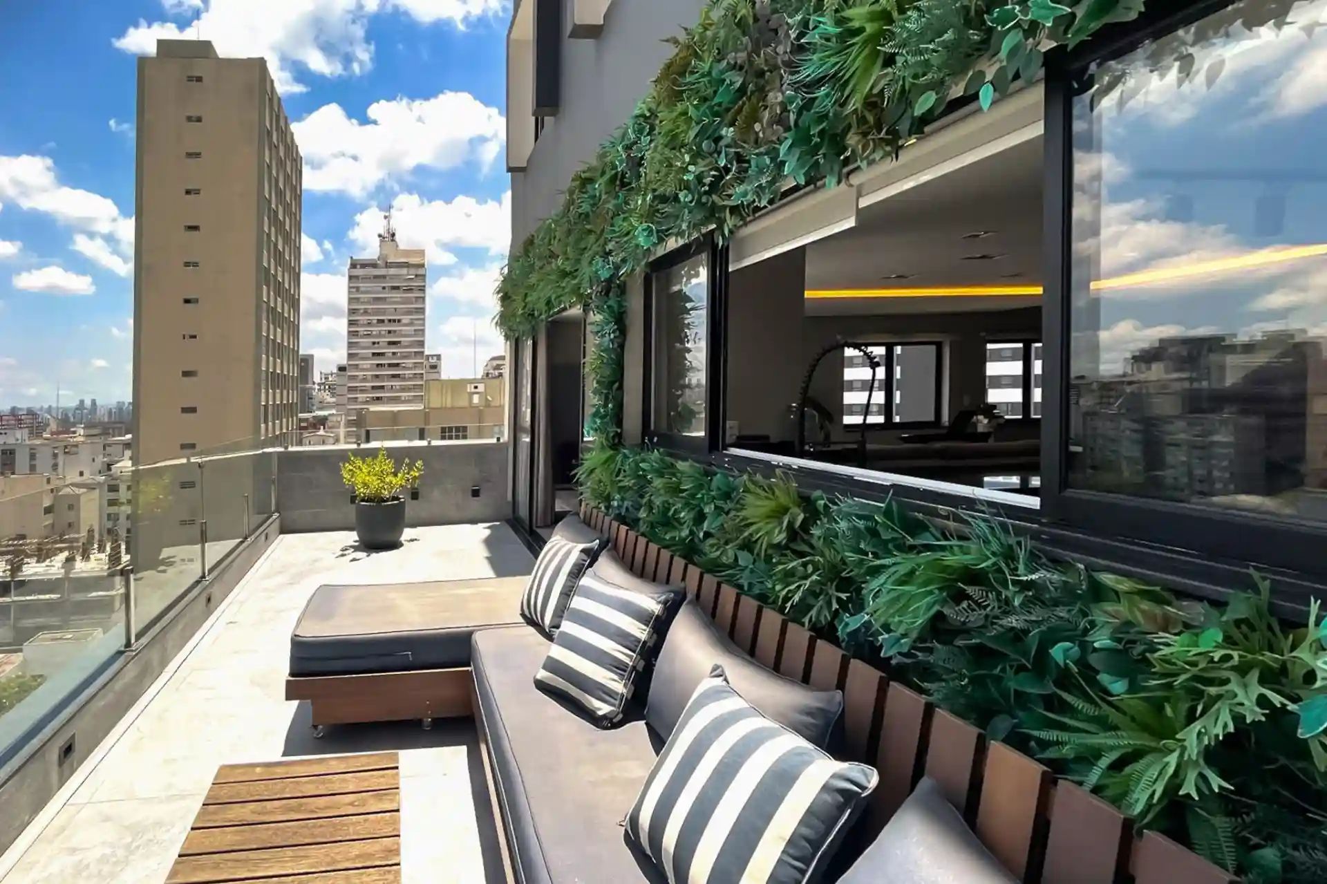 Apartamento na Rua Afonso de Freitas, com varanda moderna com decoração natural e elegante, ideal para relaxar e aproveitar a vista da cidade. Sofás confortáveis com almofadas listradas e muito verde!