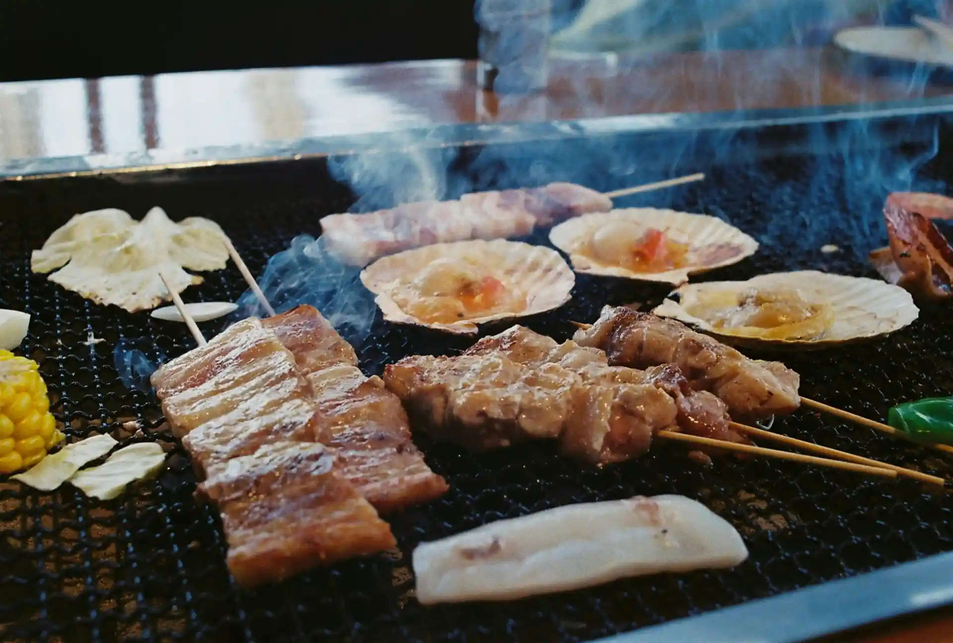 Yakitori: Deliciosas carnes grelhadas e frutos do mar sendo preparados na chapa, com fumaça subindo. Uma mistura perfeita de sabores para um churrasco.