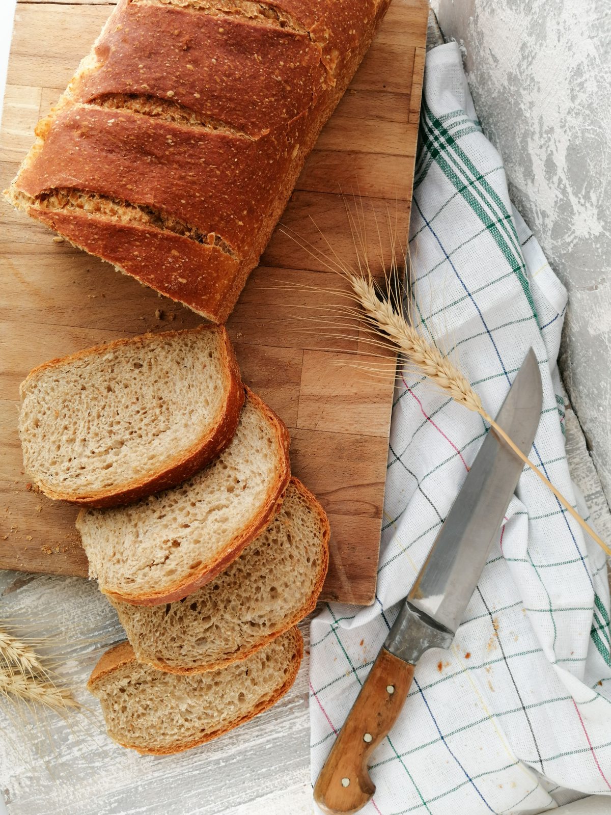 Fatias de pão artesanal de casca dourada ao lado de faca e pano de prato