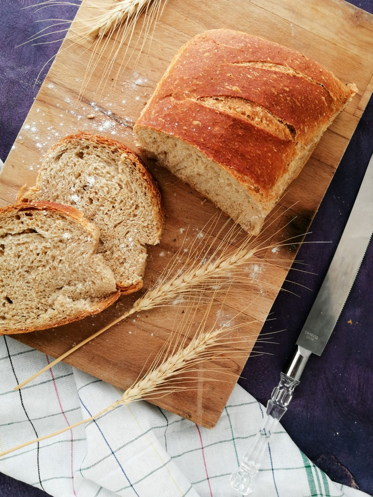 Pão artesanal de fermentação natural fatiado sobre tábua de madeira, com espigas de trigo